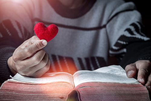 Holding Red heart in hand with Bible on wooden table, Close up, love of christian concept.